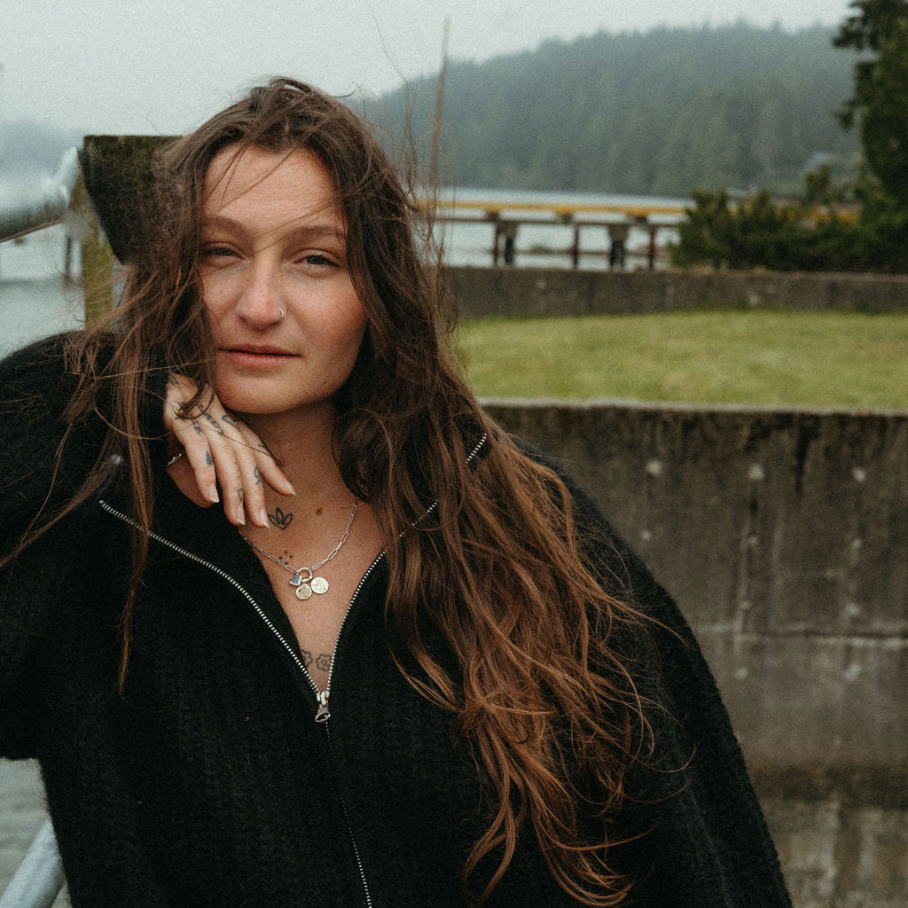 Woman with long hair standing outdoors near a body of water on a foggy day