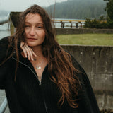Woman with long hair standing outdoors near a body of water on a foggy day