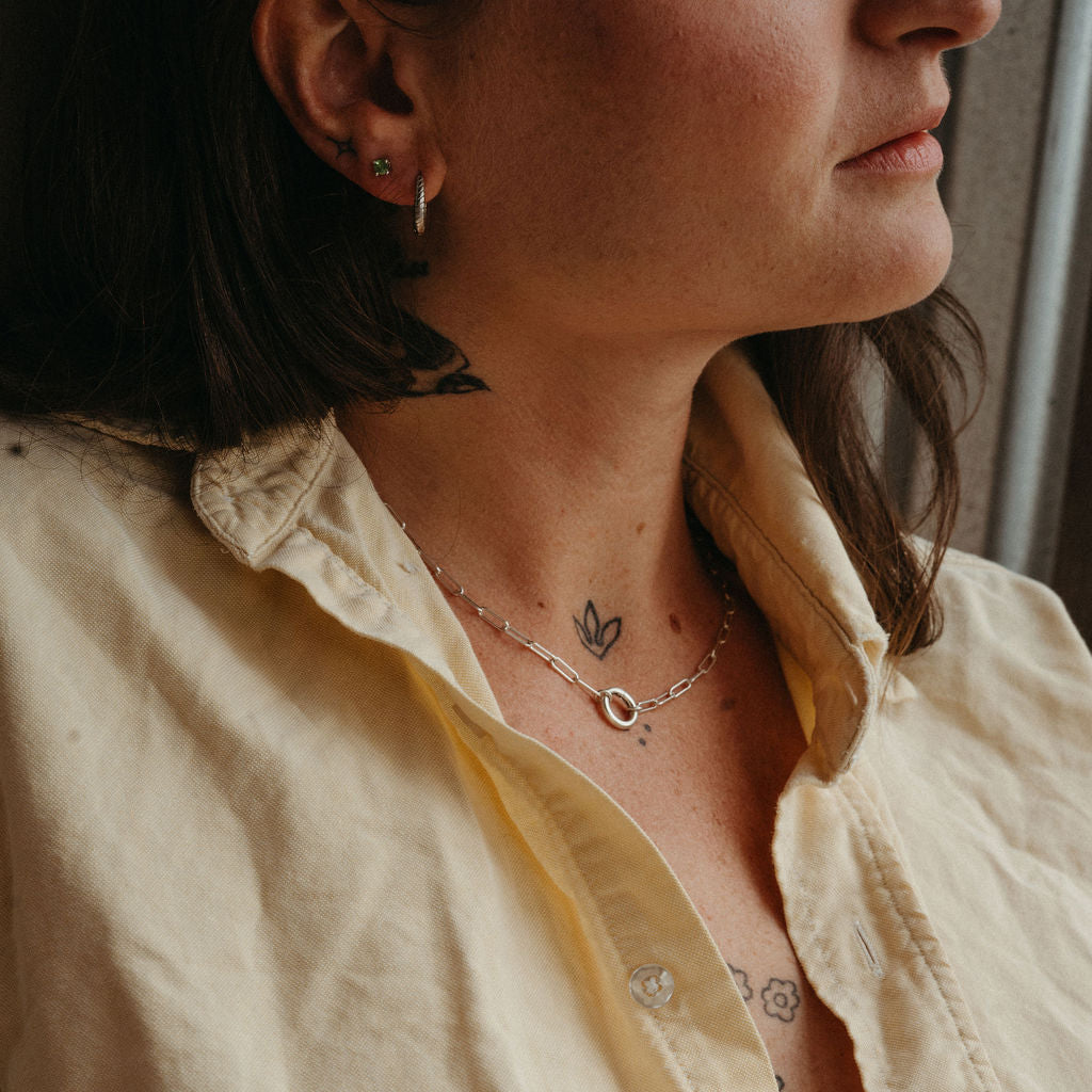 Close-up of a person wearing multiple necklaces and earrings with tattoos on their arm.