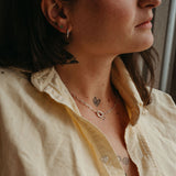 Close-up of a person wearing multiple necklaces and earrings with tattoos on their arm.