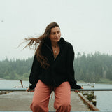 Woman sitting on a railing by a body of water with trees in the background
