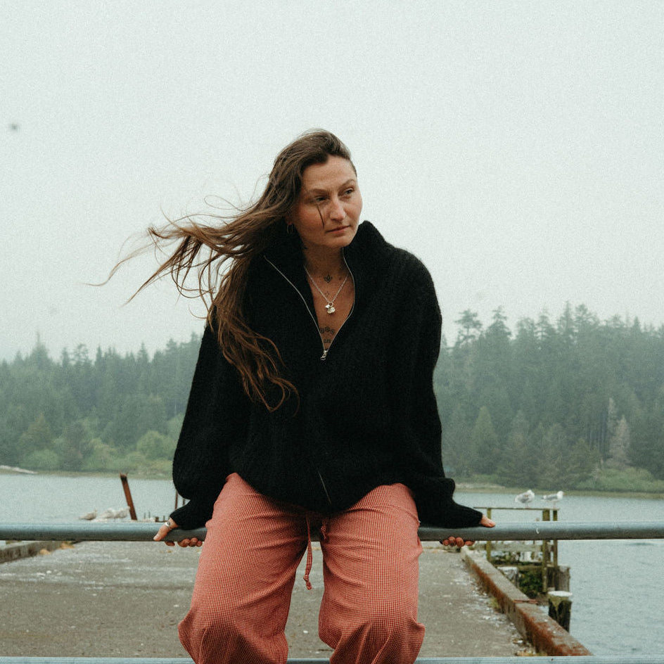 Woman sitting on a railing by a body of water with trees in the background