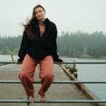 Person sitting on a railing by a body of water with trees in the background