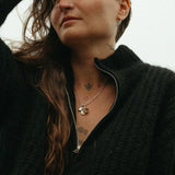 Person wearing a black jacket with visible necklaces and tattoos.