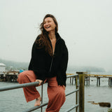 Woman sitting on a railing by a body of water with a foggy background