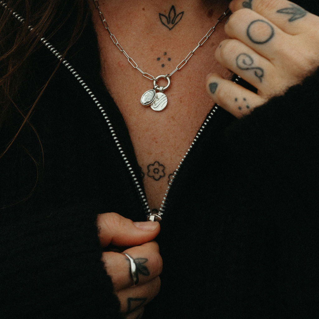 Person wearing a black jacket with visible tattoos on neck, chest, and arm.