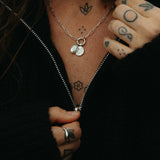 Person wearing a black jacket with visible tattoos on neck, chest, and arm.