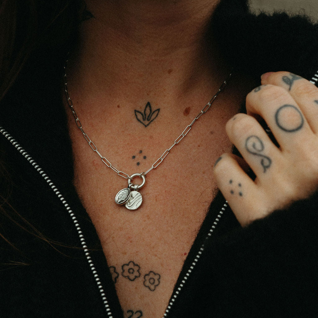 Close-up of a person's neck with a necklace, tattoos, and a black jacket.