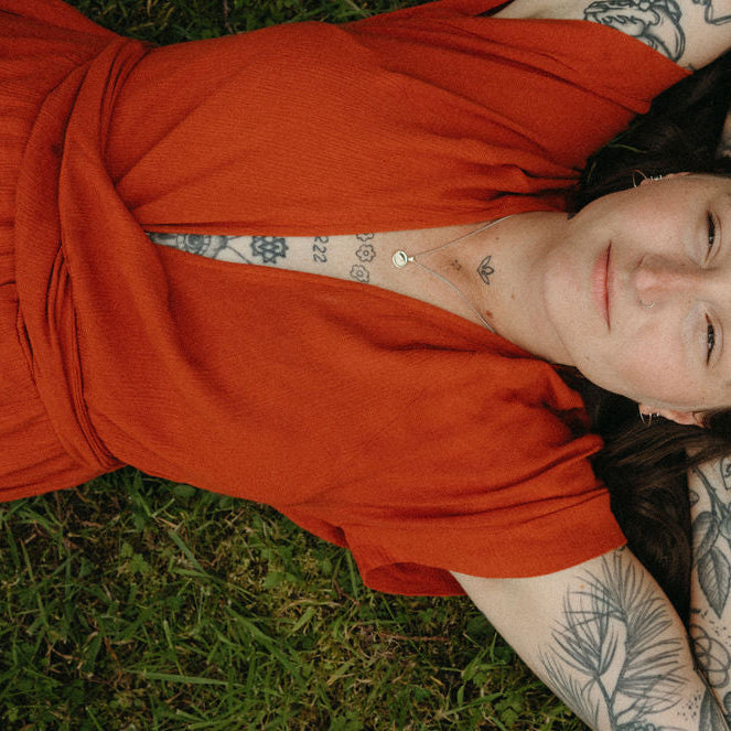 Person with tattoos lying on grass wearing an orange dress