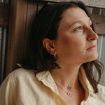 Woman wearing a yellow shirt with visible jewelry, sitting against a wooden background
