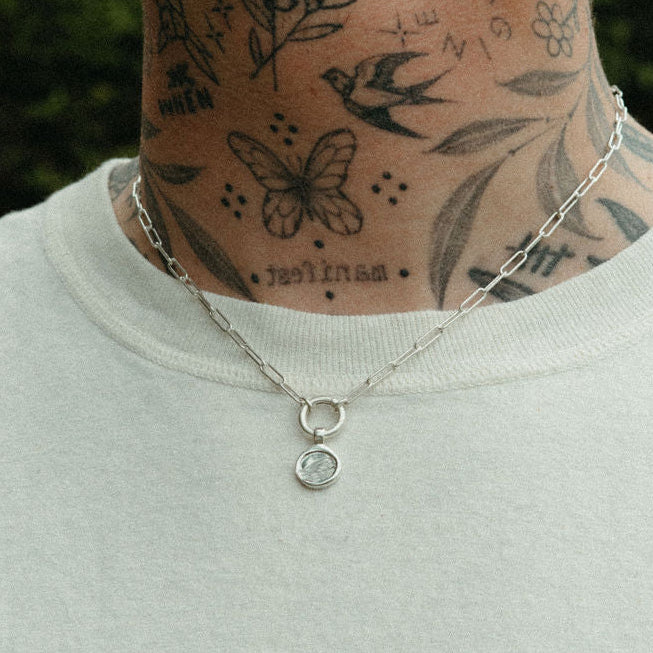 Person wearing a light gray shirt with visible neck tattoos and a necklace.