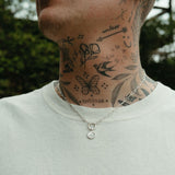 Person wearing a light gray shirt with visible neck tattoos and a silver necklace.