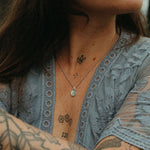 Woman with tattoos wearing a blue lace top by a body of water