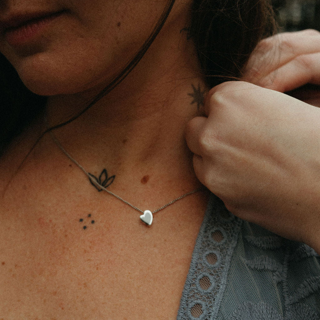 Person wearing a necklace with a heart pendant, surrounded by tattoos on their skin.