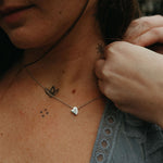 Person wearing a necklace with a heart pendant, surrounded by tattoos on their skin.