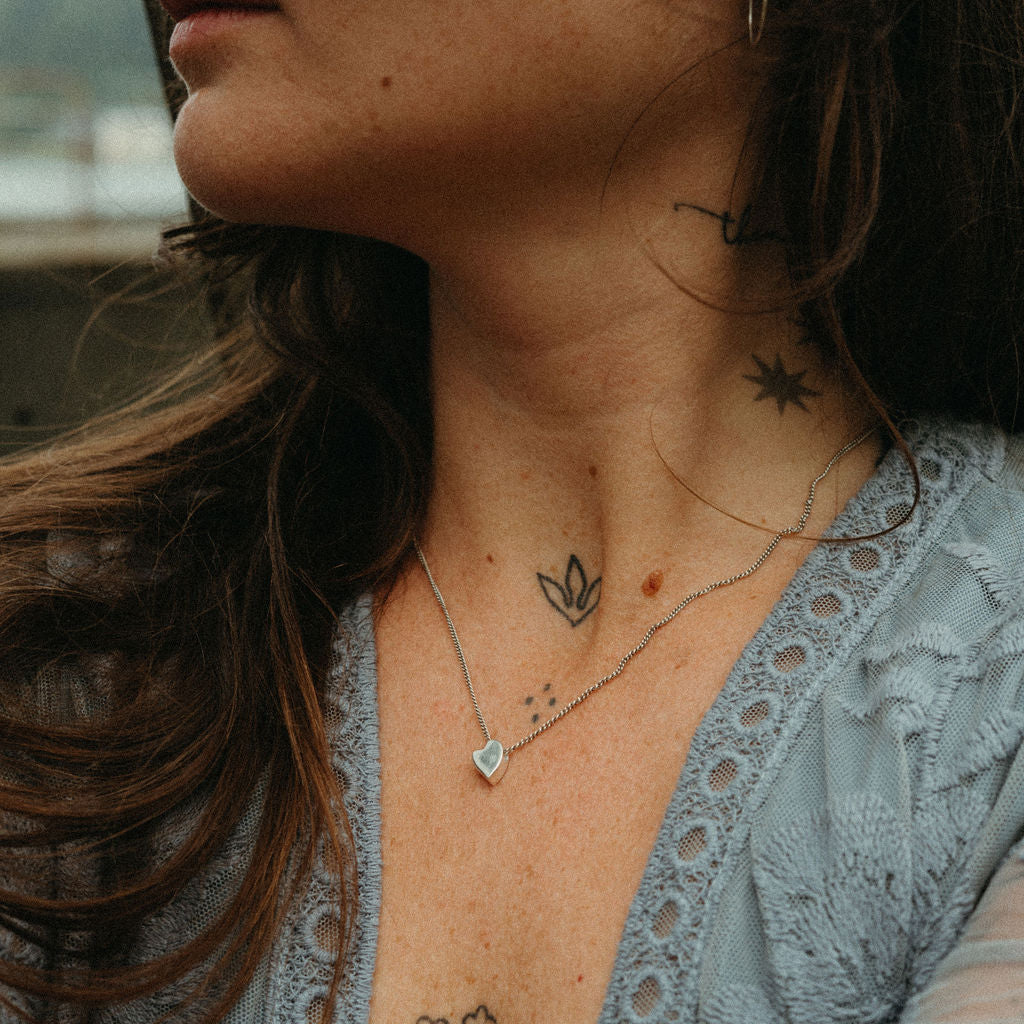 Close-up of a person with tattoos and necklaces, wearing a light blue lace top.
