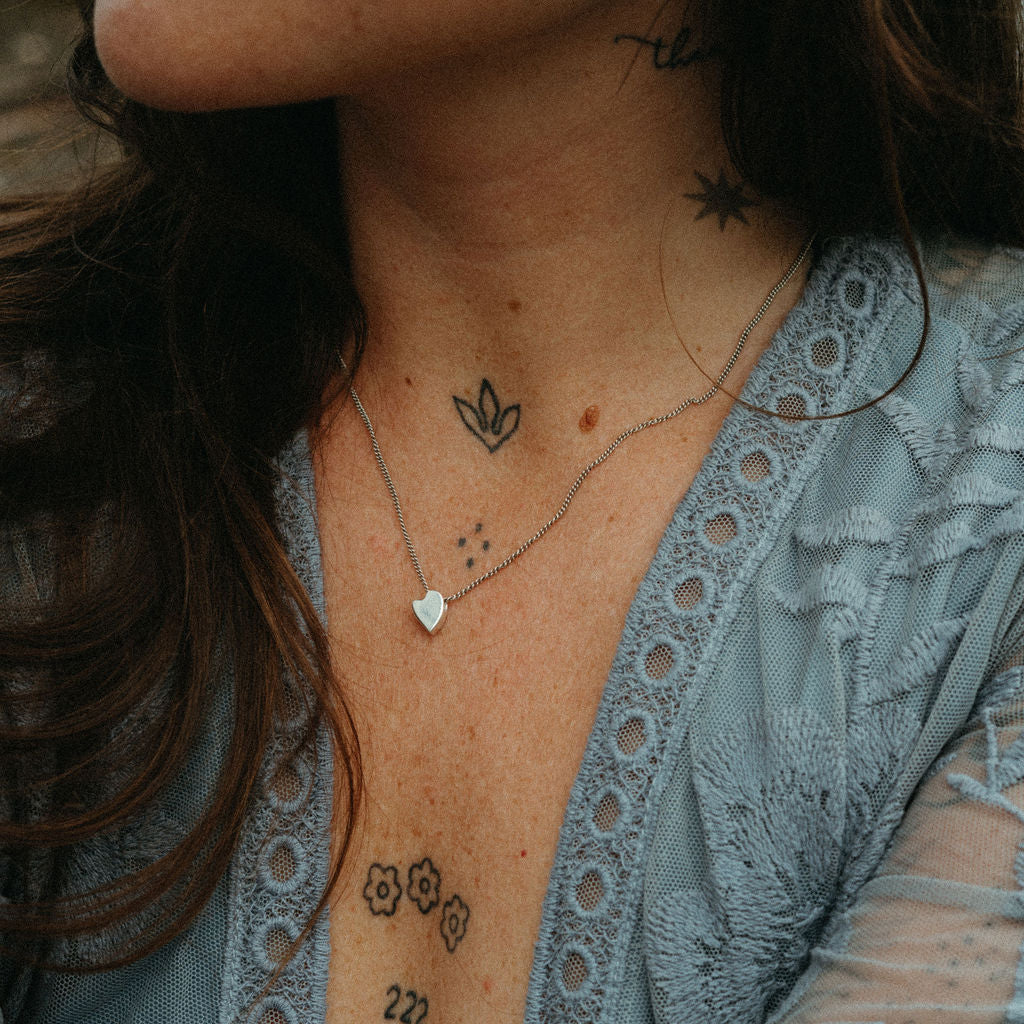 Close-up of a person wearing a blue lace top with visible tattoos on their neck, chest, and arms.