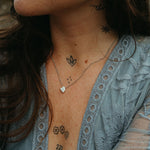 Close-up of a person wearing a blue lace top with visible tattoos on their neck, chest, and arms.