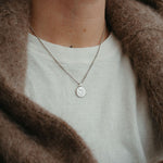 Necklace with a moyeha pendant worn by a person in a brown coat and white shirt.