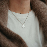 Necklace with a moyeha pendant worn by a person in a brown coat and white shirt.
