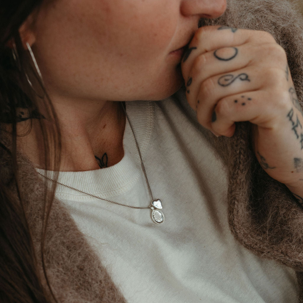 Person wearing a necklace with a heart pendant, holding their head with one hand.