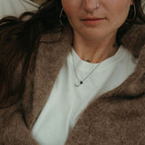 Woman wearing a brown coat over a white shirt with visible tattoos on her arms.