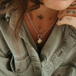 Person wearing a light green denim jacket with a necklace and tattoos visible.