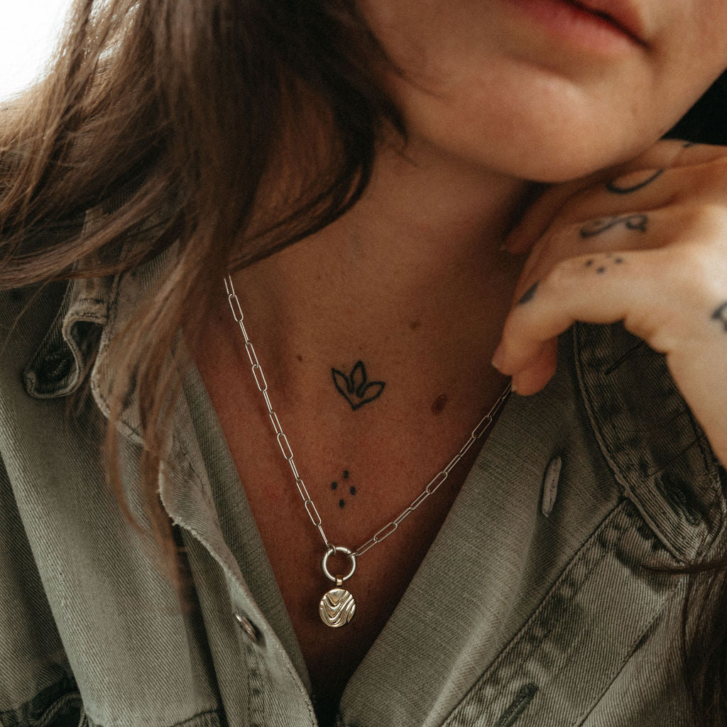 Person wearing a green jacket with a necklace and visible tattoos.