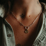 Necklace with a pendant worn by a person, showing tattoos on the neck and shoulders.