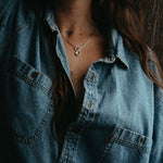 Person wearing a denim shirt with a necklace, against a dark background