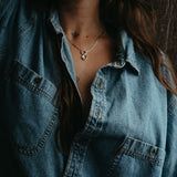 Person wearing a denim shirt with a necklace, against a dark background