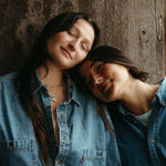 Two people wearing denim shirts against a wooden wall.