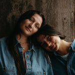 Two people wearing denim shirts against a wooden wall.