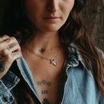 Woman with tattoos and a necklace, wearing a denim jacket, against a wooden background.