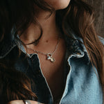 Woman with tattoos on her hands wearing a denim shirt against a wooden background, wearing the heart and gold plated lupine pendants. 