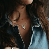 Woman with tattoos on her hands wearing a denim shirt against a wooden background, wearing the heart and gold plated lupine pendants. 