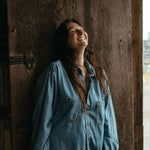 Woman in a denim shirt standing against a wooden door