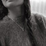 Black and white photo of a person wearing a textured sweater and a heart pendant necklace.