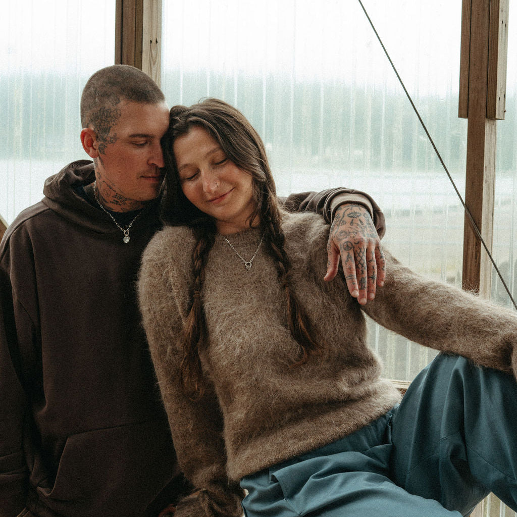 Two people sitting close together in a greenhouse with large windows.