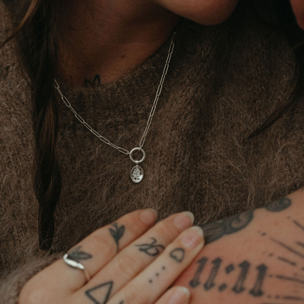 Close-up of a person wearing a necklace with a pendant, holding hands with another person with tattoos.