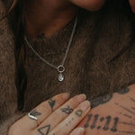 Close-up of a person wearing a necklace with a pendant, holding hands with another person with tattoos.