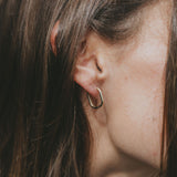 A close-up side profile of a person with long brown hair wearing a small gold hoop earring.