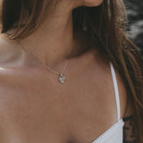 A close-up lifestyle shot of a woman wearing a delicate gold chain necklace with a small circular pendant, paired with a white spaghetti strap top.