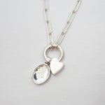Silver necklace with a heart-shaped pendant and a Lupine pendant on a light gray background