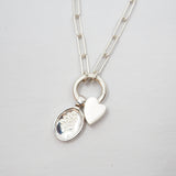 Silver necklace with a heart-shaped pendant and a Lupine pendant on a light gray background