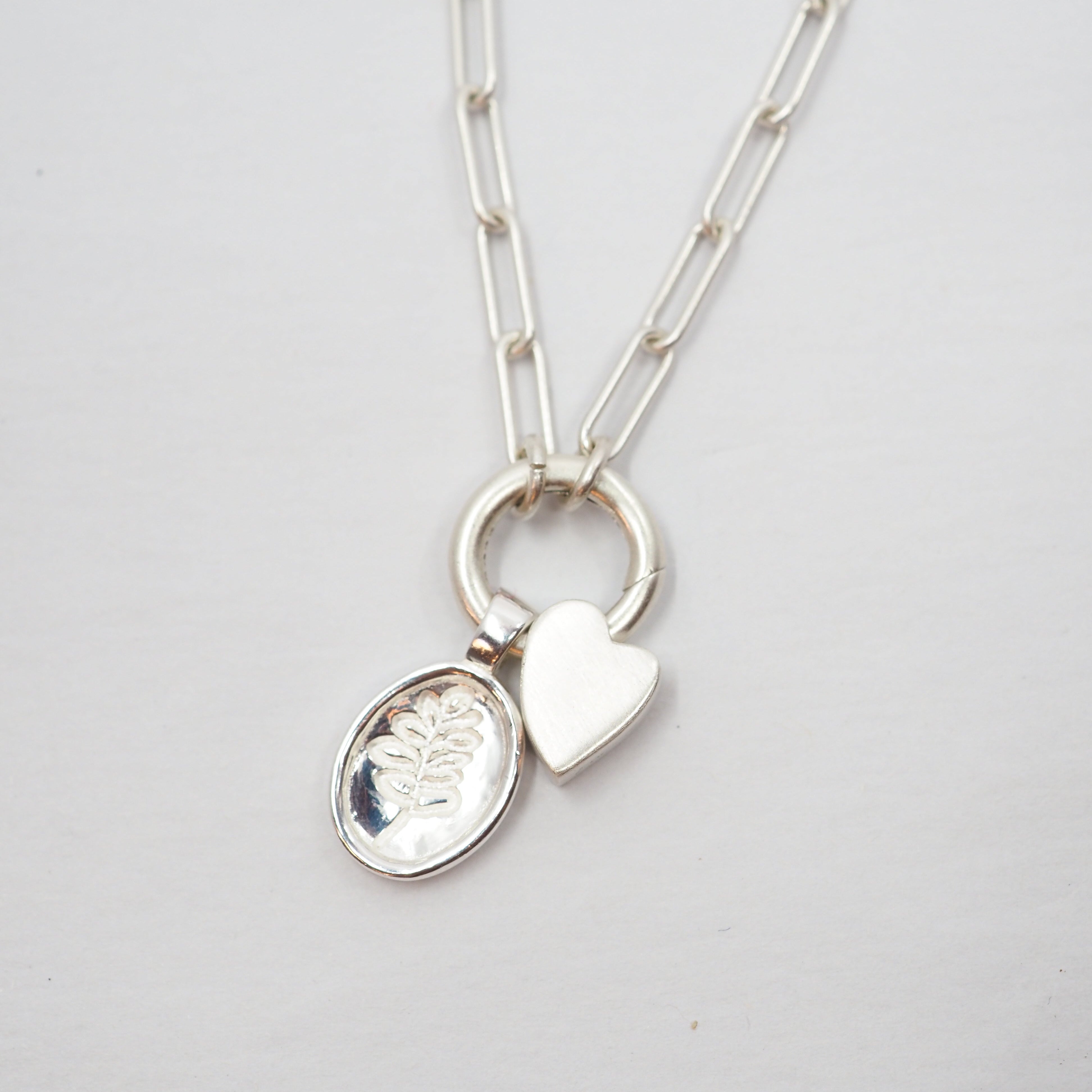 Silver necklace with a heart-shaped pendant and a Lupine pendant on a light gray background