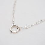 Silver necklace with a circular charm connector on a light gray background