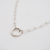 Silver necklace with a circular charm connector on a light gray background