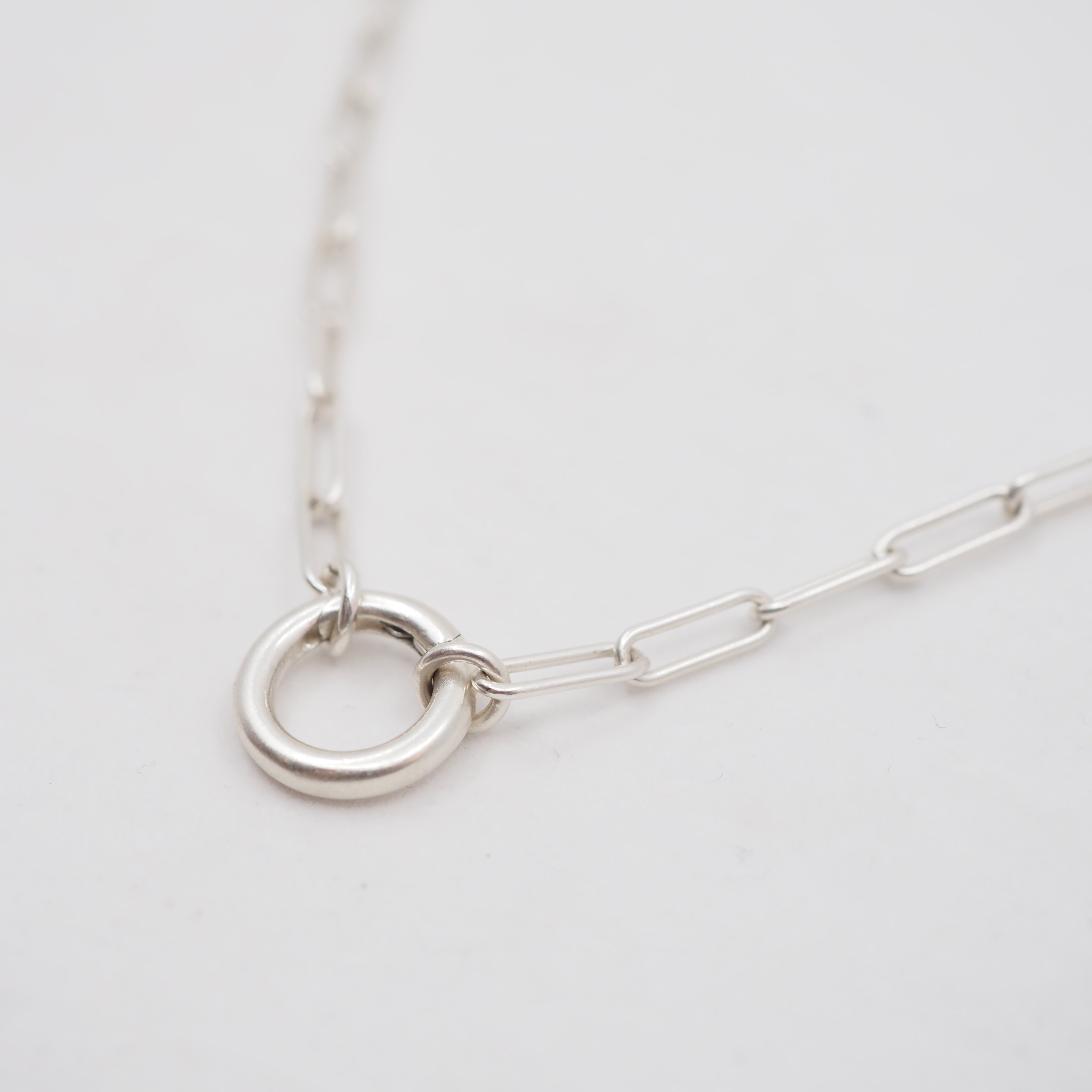 Silver necklace with a circular charm connector on a light gray background