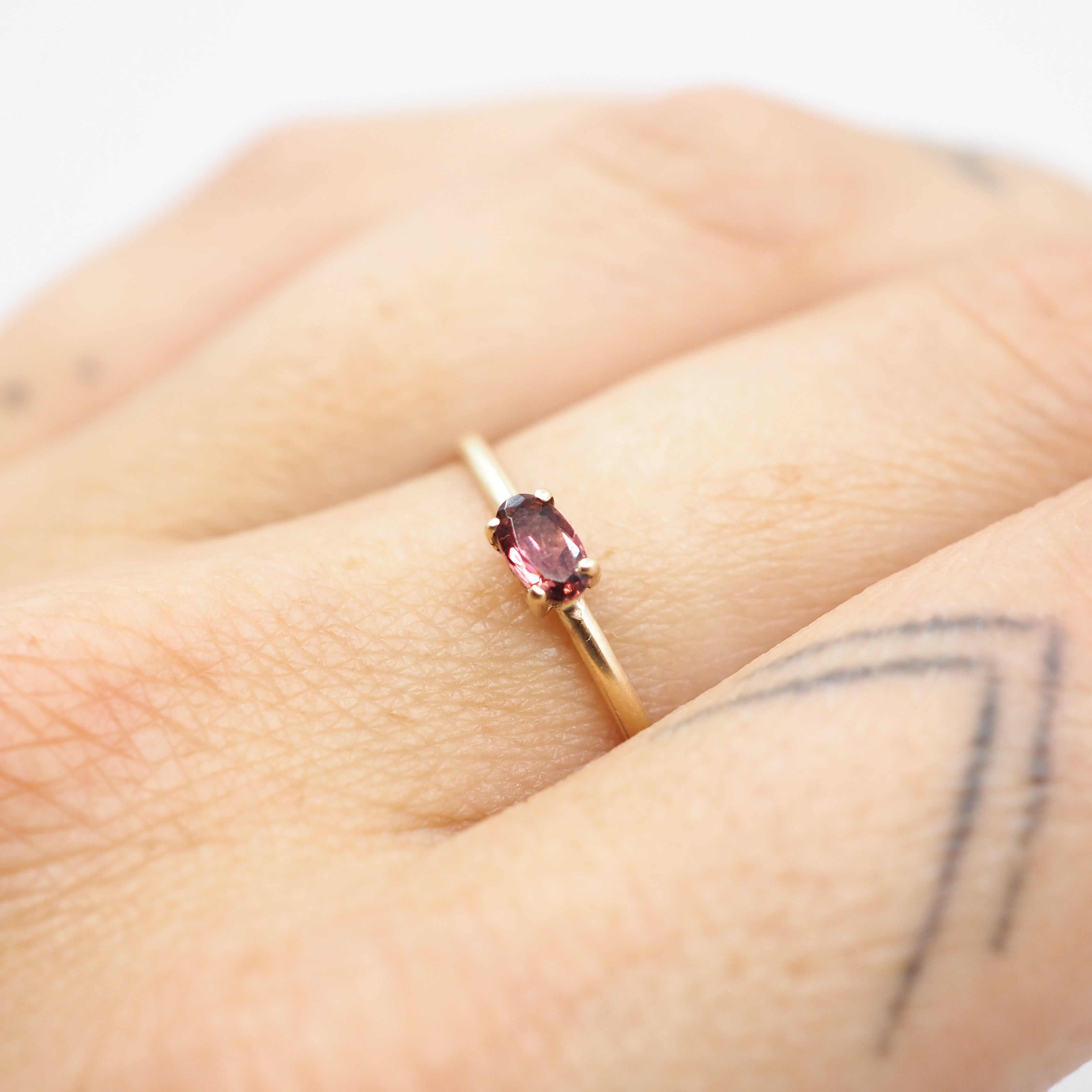 A close-up of a gold ring with an oval pink gemstone worn on a person's finger.